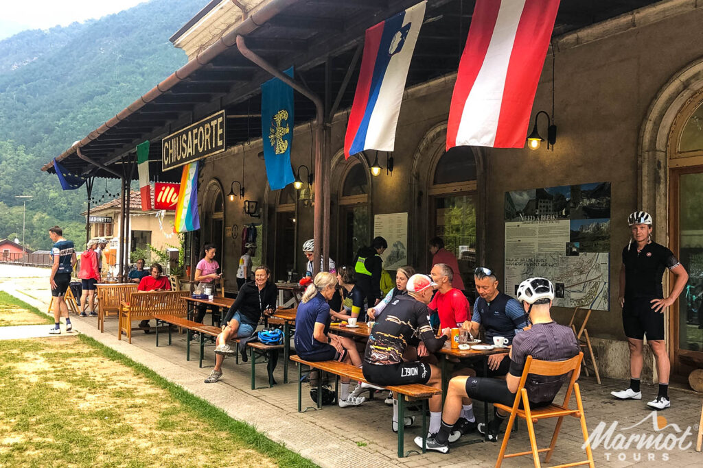 Group of cyclists enjoying rest stop at colourful cafe adorned with flags on guided road cycling tour Slovenia with Marmot Tours