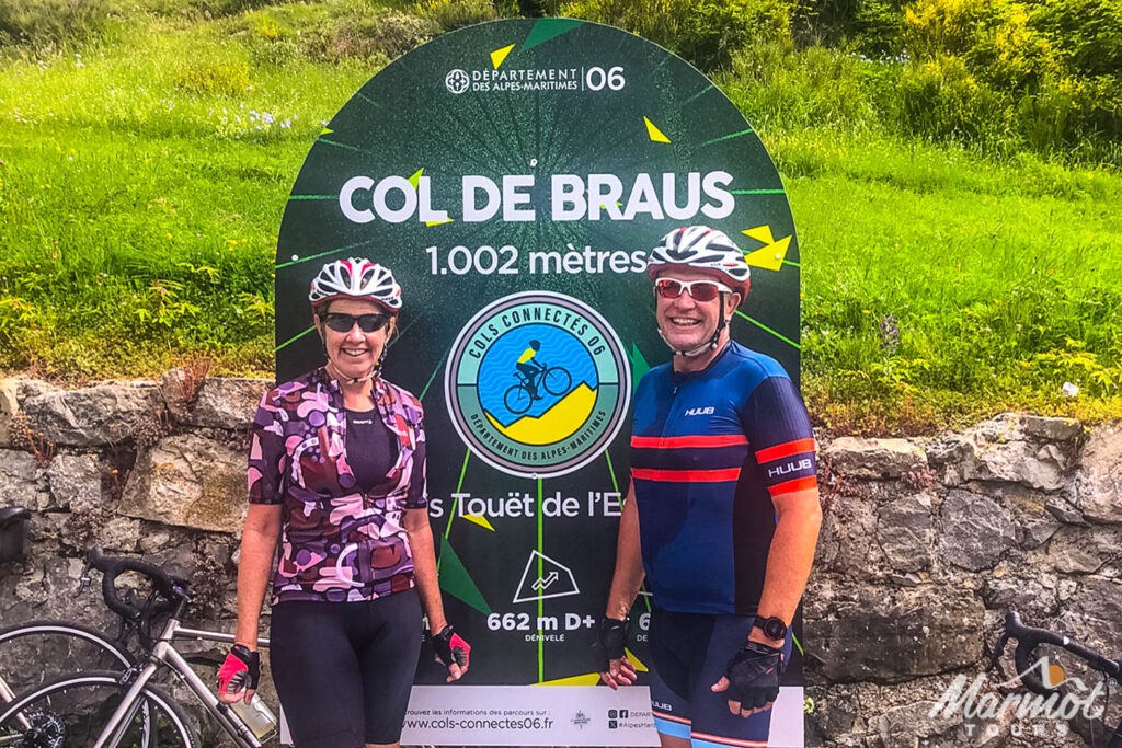 Pair of cyclists smiling at the Col de Braus col sign on guided road cycling tour southern Alps with Marmot Tours