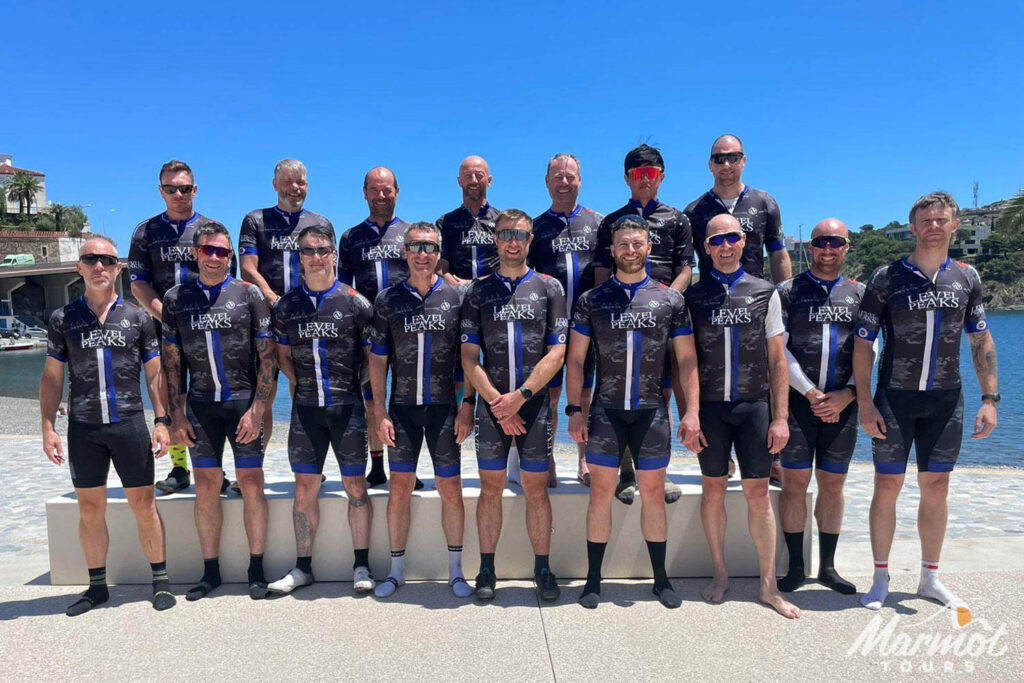 Group of 16 cyclists on shore of Mediterranean having completed Raid Pyrenean cycling challenge with Marmot Tours