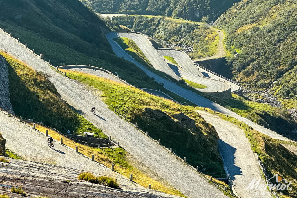 St Gotthard pass cobbles snaking up the mountainside with cyclists riding on Marmot Tours