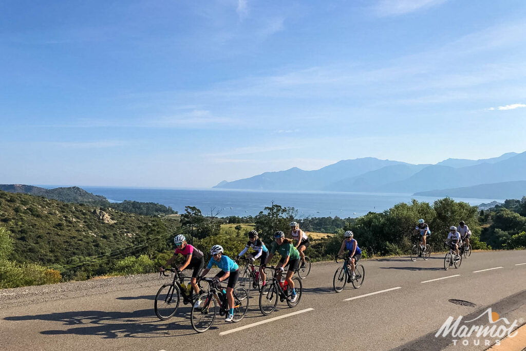 Group of cyclists on sunny coast road on guided cycling tour of Corsica with Marmot Tours