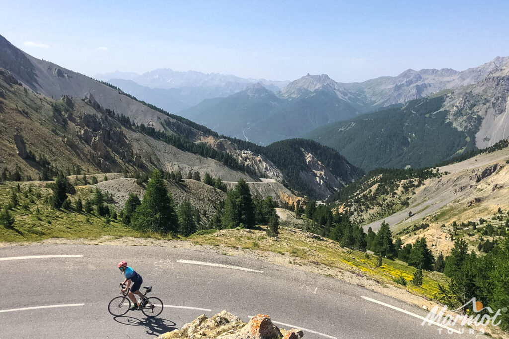 Cyclist climbing hairpin bend on Raid Alpine with mountainous backdrop on Marmot Tours guided cycling holiday French Alps