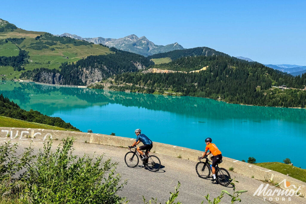 Pair of cyclists on Cormet de Roselend climb on French Alps cycling holiday with Marmot Tours with Lac du Roselend backdrop