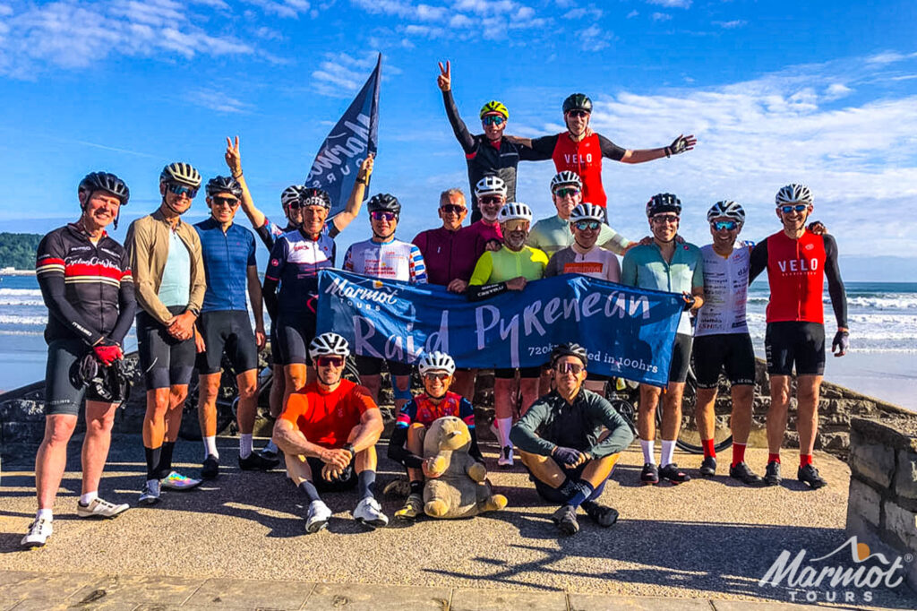 Group of cyclists and Marmot Tours Raid Pyrenean banner on Atlantic beach