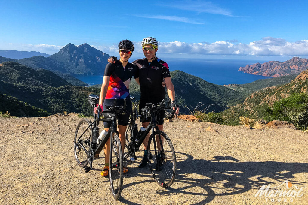 Pair of cyclists smiling with coastal backdrop on Raid Corsica guided road cycling tour with Marmot Tours