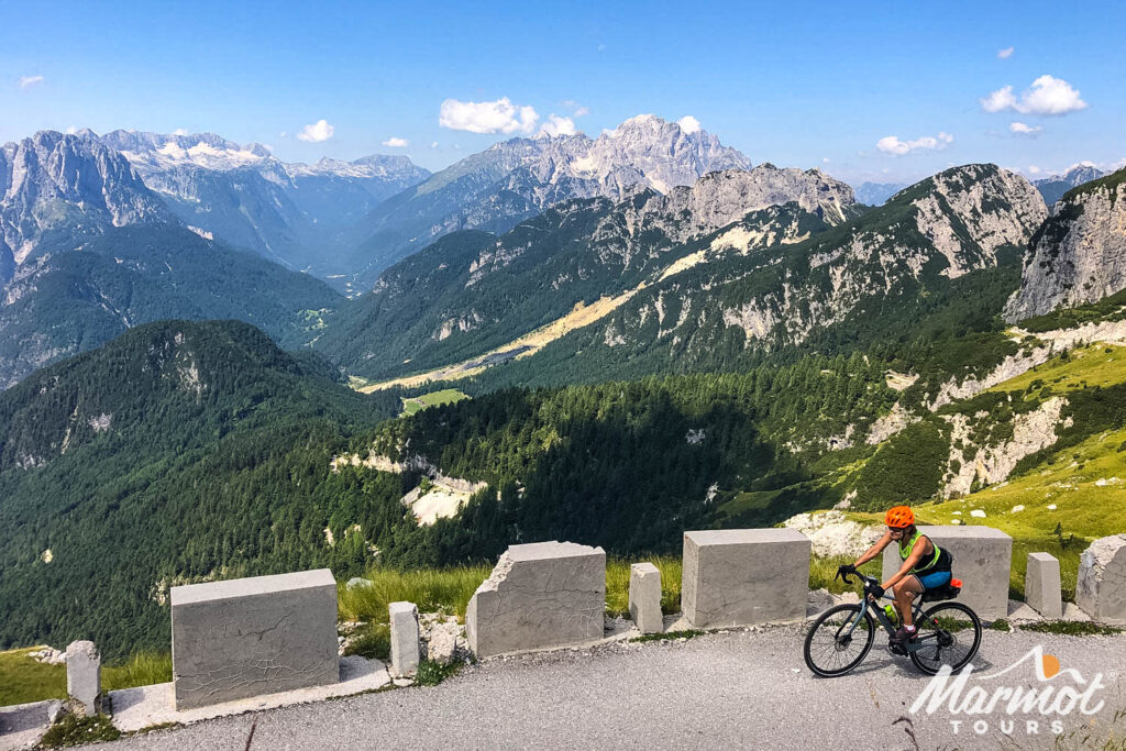 Female cyclist riding balcony road of on Mangart Saddle cycling climb with mountainous backdrop on Slovenia guided cycling holiday with Marmot Tours