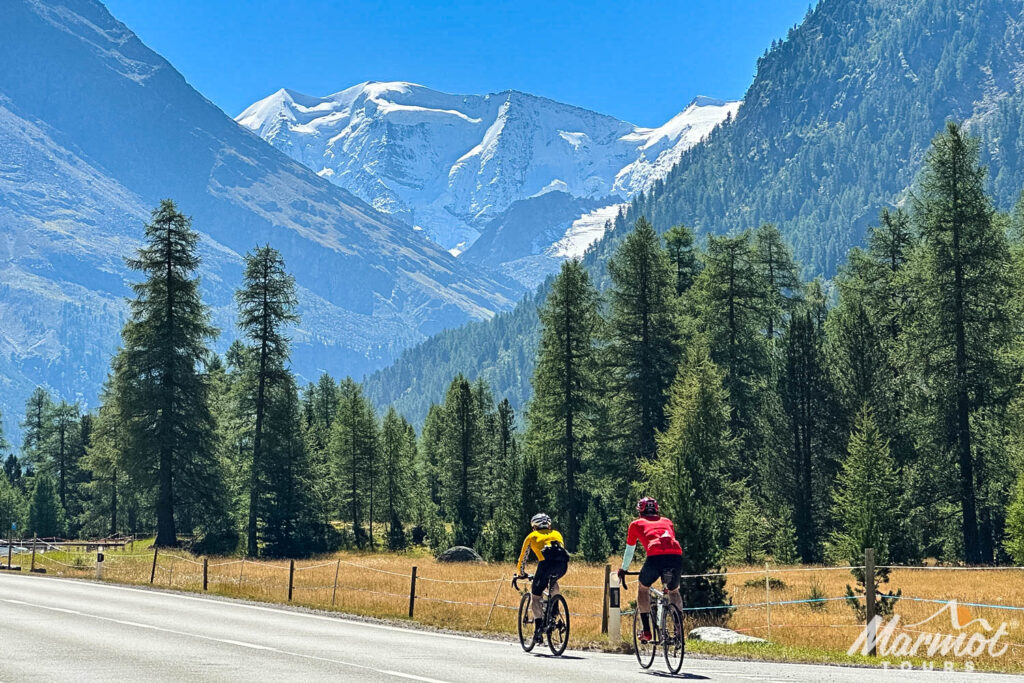 Pair of cyclists on road passing beneath glacier on guided road cycling holiday in the Swiss Alps with Marmot Tours