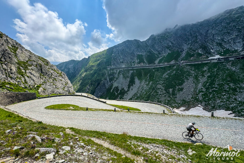 Cyclist climbing cobbles of Tremola road on Sankt Gotthard Pass in Swiss Alps with Marmot Tours