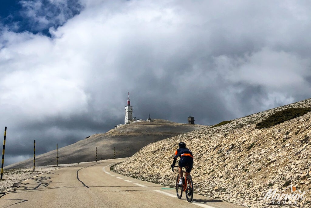 Cyclist climbing Mont Ventoux with weather beacon summit ahead under cloudy sky on Marmot Tours road cycling holiday