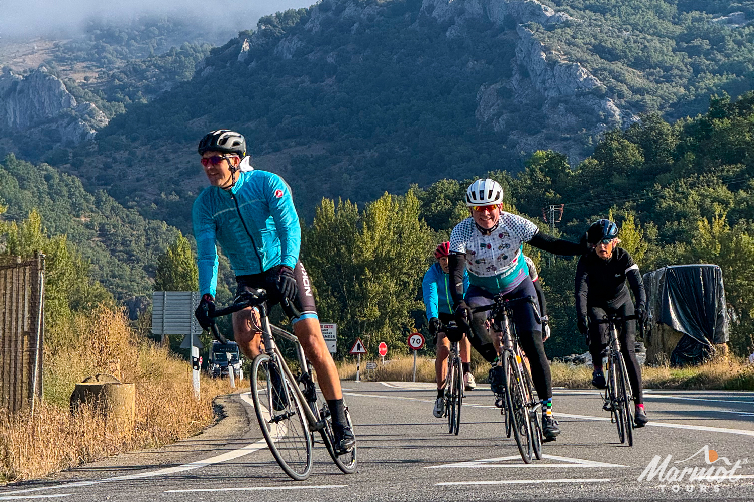 Group of cyclists descending and waving with forested slope backdrop in the Picos of northern Spain with Marmot Tours