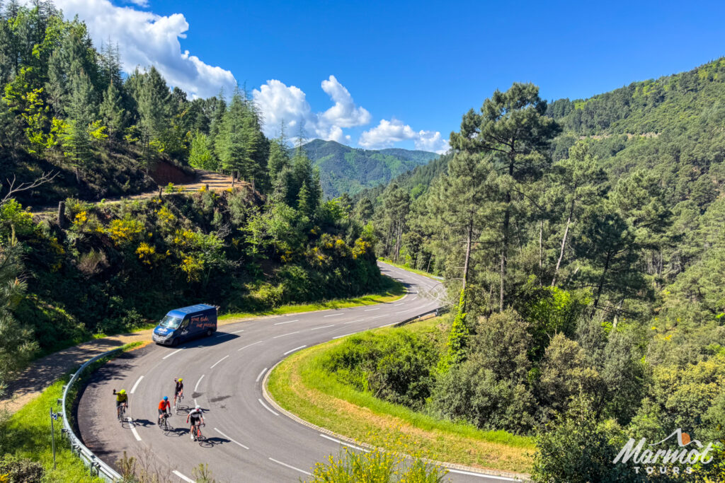 Group of cyclists wave on hairpin bend passing Marmot Tours support van on guided group cycling holiday in Cevennes and Ardeche South of France