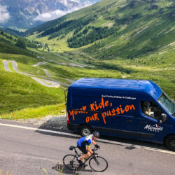 Cyclist riding past Marmot Tours support vehicle on mountain climb with hairpin bends background