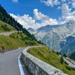Group of cyclists climb Passo dello Stelvio hairpin bends on Marmot Tours guided road cycling holiday Italian Dolomites Swiss Alps with snowy peaks background