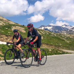 Pair of female cyclists climbing mountain pass with snowy mountains background on Marmot Tours guided road cycling holiday Swiss Alps and Italian Dolomites