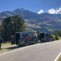 Marmot Tours guide roadside with pair of liveried support vehicles with mountains backdrop on guided road cycling tour Swiss Alps and Italian Dolomites