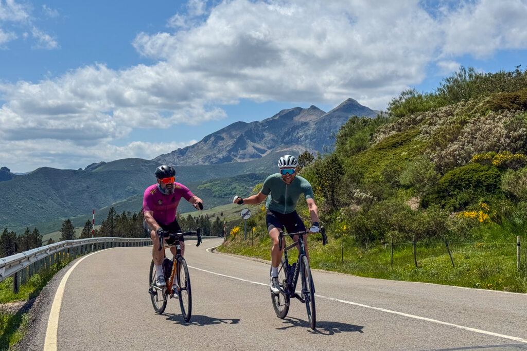 Pair of cyclists fist bump with mountain backdrop on cycling holiday in Picos and Asturias with Marmot Tours