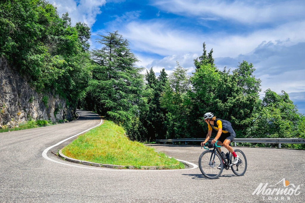 cyclist rounding hairpin bend on forested slope of monte grappa from semonzo on marmot tours guided road cycling holiday dolomites