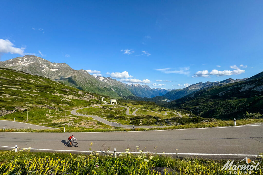 Cyclists climbing Passo San Bernadino with field of hairpin bends and snowy mountain peaks in distance on Marmot Tours guided road cycling tour Italian Dolomites