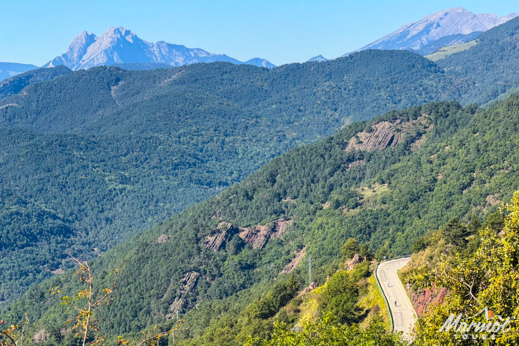 Cyclist on mountain road with high mountains backdrop and forested slopes on guided cycling holiday Catalonia northern Spain with marmot tours
