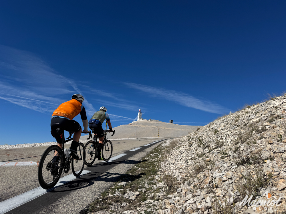 Pair of cyclists climbing Mont Ventoux with summit in sight on blue sky day