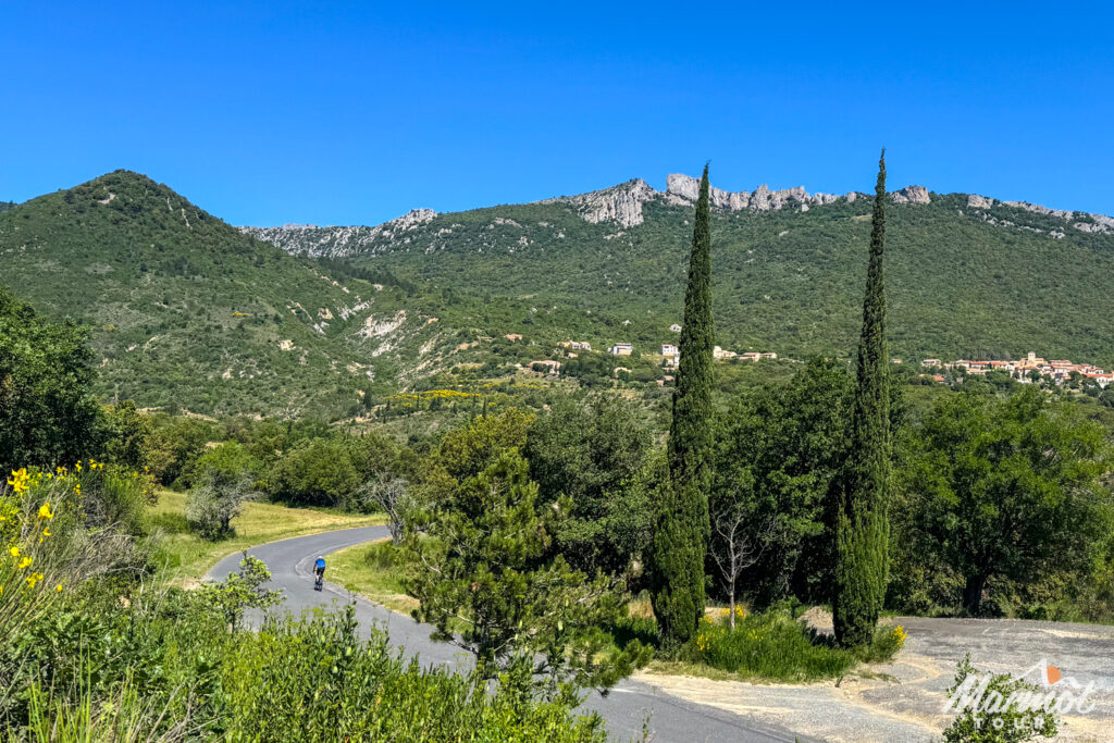 Cyclist on quiet rural road with rocky cliff edge and poplar trees on guided road cycling holiday French Pyrenees with Marmot Tours