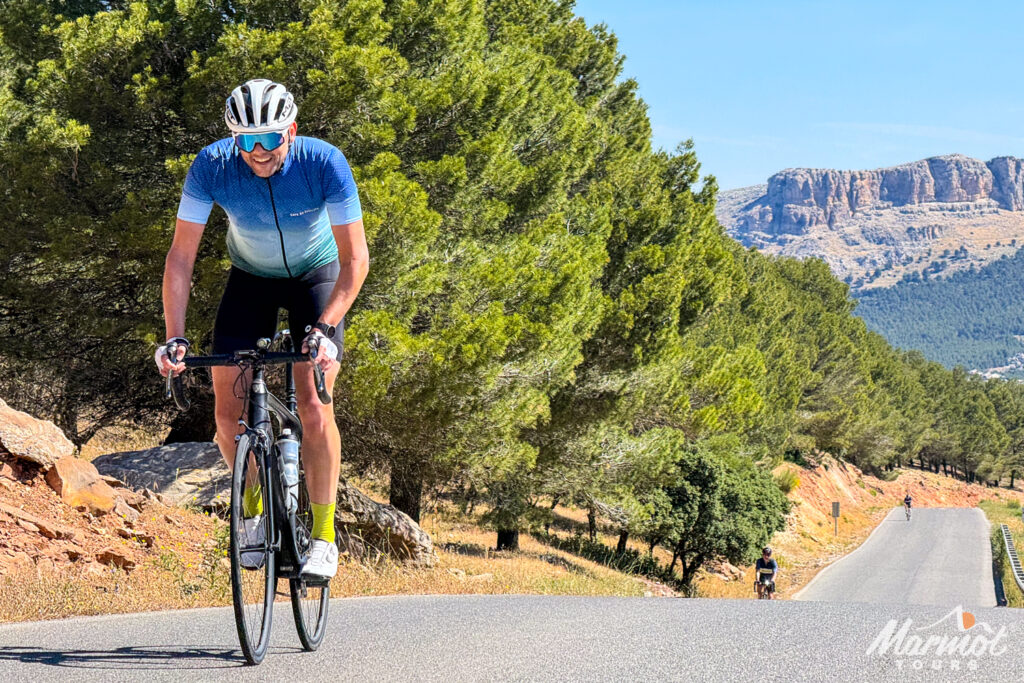 Cyclists climbing hilly road with mountains backdrop on guided road cycling holiday southern Spain Andalusia with Marmot Tours in spring